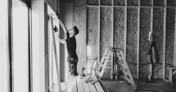 Black and white photo of a worker installing drywall indoors, Falun, Sweden. man doing construction work inside house