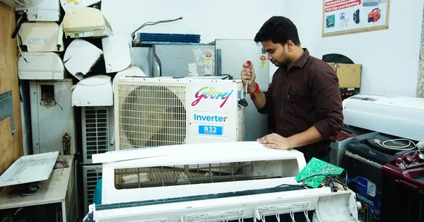 Technician repairing an air conditioner unit in New Delhi workshop. air conditioner repair technician in workshop