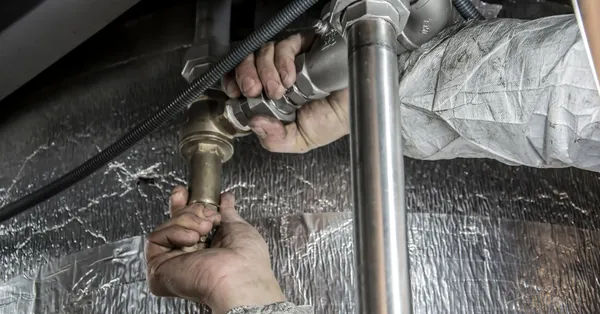 Close-up of a plumber's hands installing steel pipes indoors, showcasing skilled manual work. plumber installs pipe fittings