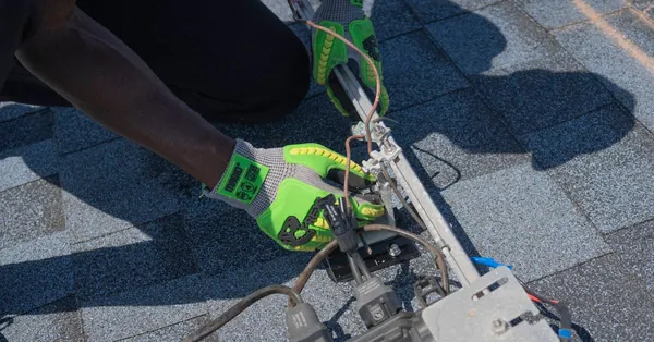 Close-up of a technician working on solar panel installation with green gloves in Tampa, Florida. technician installing solar panels on rooftop