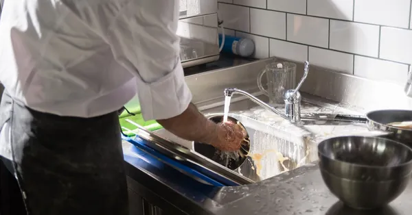 A chef washing dishes at a sink in a bright, modern kitchen setting. a person washing dishes in the sink