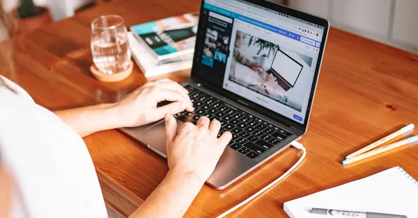 A person working remotely on a laptop at a wooden desk with stationery and a notepad. person using laptop on wooden desk