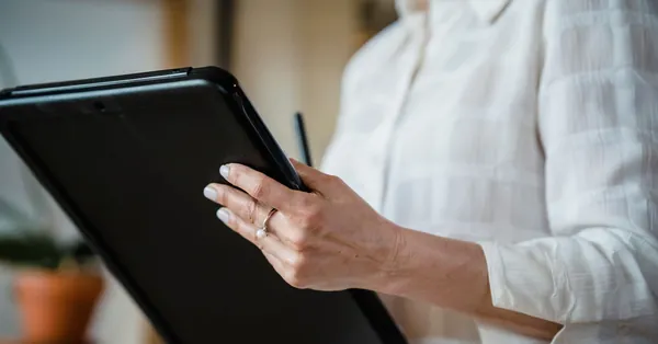 Close-up of a woman holding a digital tablet in an office environment, focusing on hand details. woman holding folder