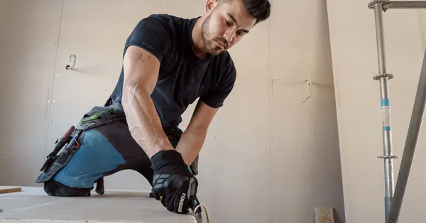 Man in gloves cutting plasterboard for drywall installation inside a building. man cutting a plasterboard