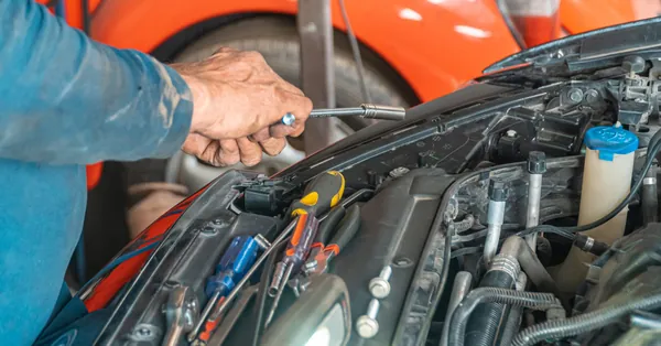 Mechanic performing maintenance on a car engine in a garage setting, using various tools. car mechanic holding a tool for repair