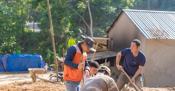 A diverse team of workers collaborates on an outdoor construction site surrounded by greenery. group of workers collaborating on outdoor construction site