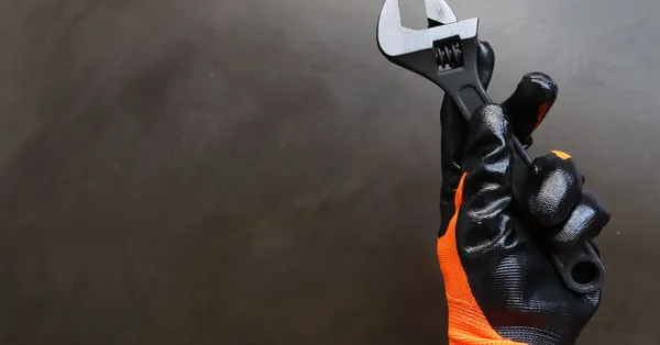 A gloved hand holding an adjustable wrench on a dark background. person holding wrench