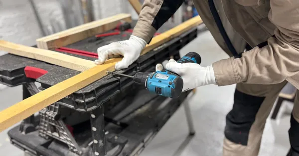 A carpenter using a power drill to work on wooden planks in an indoor workshop setting. carpenter using drill on wooden plank in workshop