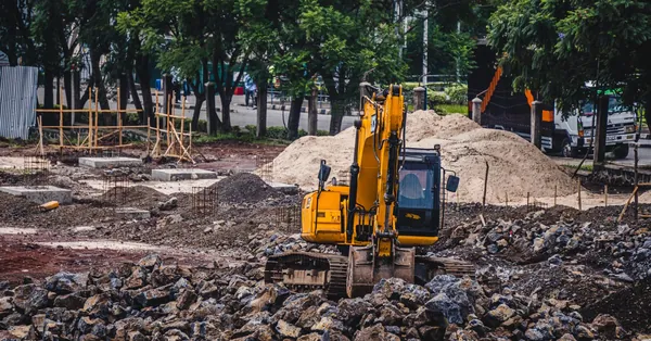 A yellow excavator working at an urban construction site surrounded by rocks and trees. yellow excavator at urban construction site
