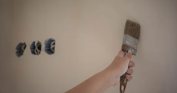 A person painting a wall with a brush, showcasing a home makeover process. person painting white wall