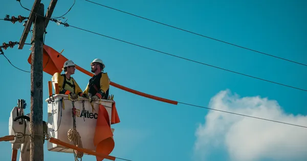 Two electricians in safety gear working on a utility pole with a clear blue sky backdrop. two electricians working on utility pole