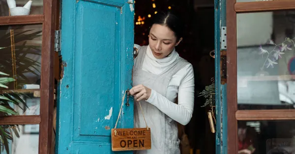 A woman adjusts an open sign on a blue wooden door of a cafe inviting customers inside. photo of woman putting wooden signage on doorknob