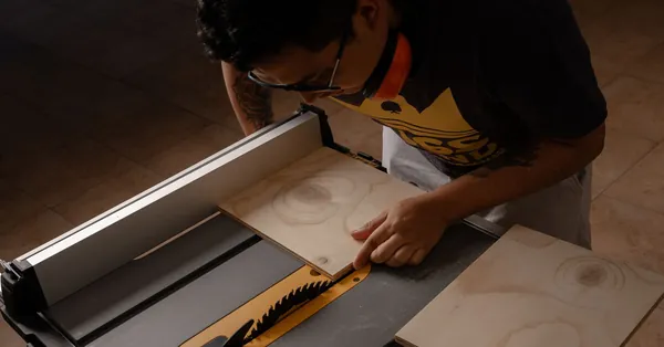 A carpenter uses a table saw to cut wooden planks in a workshop setting, demonstrating skilled woodworking. carpenter processing wood with a table saw