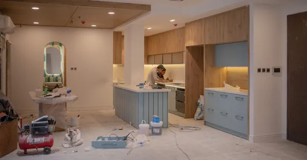 A modern kitchen undergoing renovation, featuring a worker, tools, and materials. men working inside a house under repairs