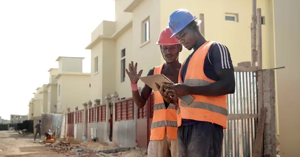 Two construction workers in helmets and vests review blueprints on a site. construction workers in helmets and reflective vests
