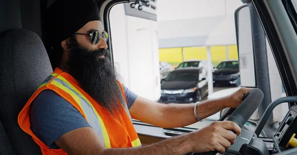 Bearded truck driver wearing a turban and safety vest inside a truck cab, focused on driving. truck driver in turban